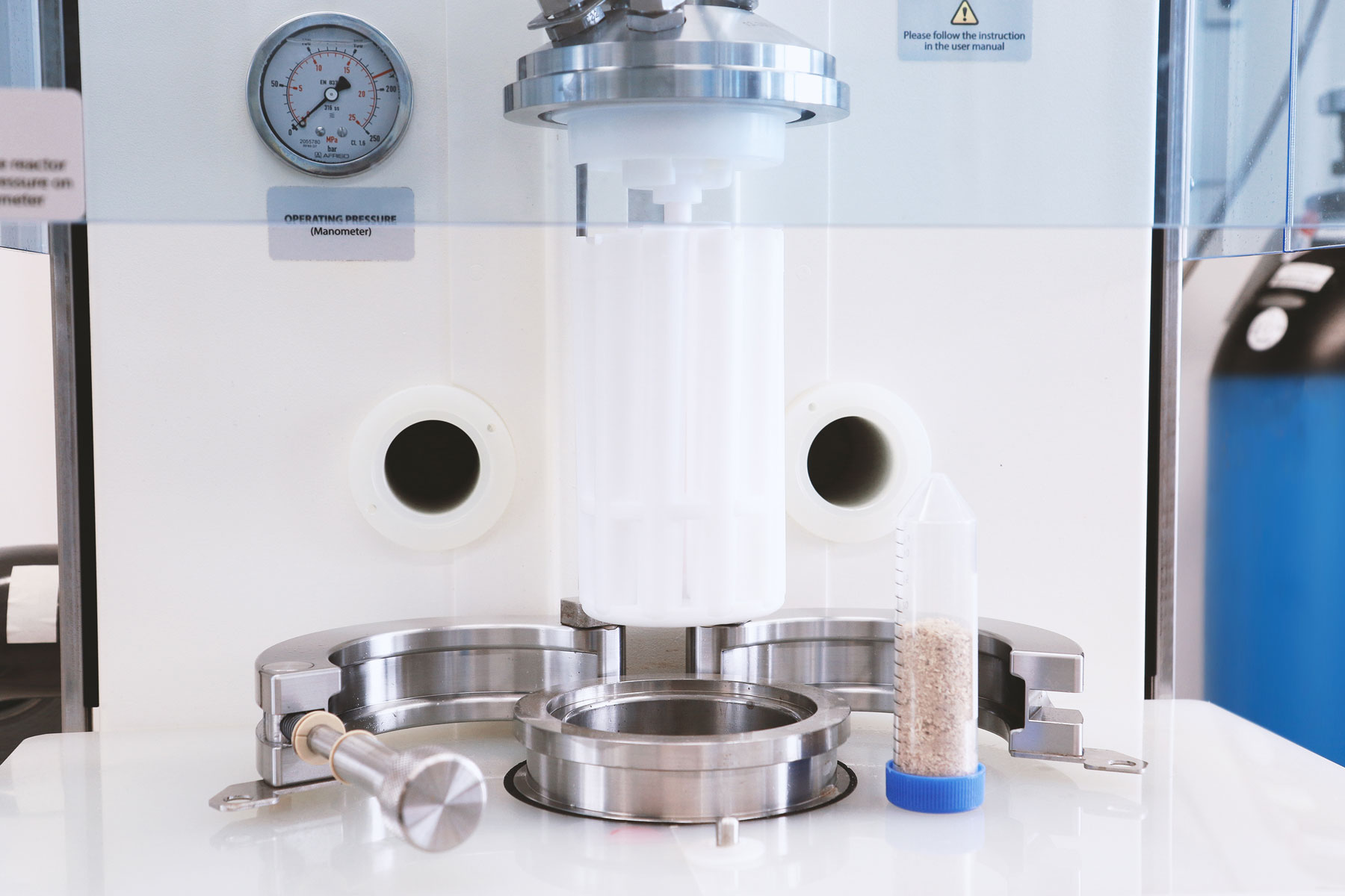 Das Foto zeigt eine Laborapparatur mit einem kolbenförmigen Druckbehälter und daneben einen Messbehälter, der mit feinen Holzspänen gefüllt ist.