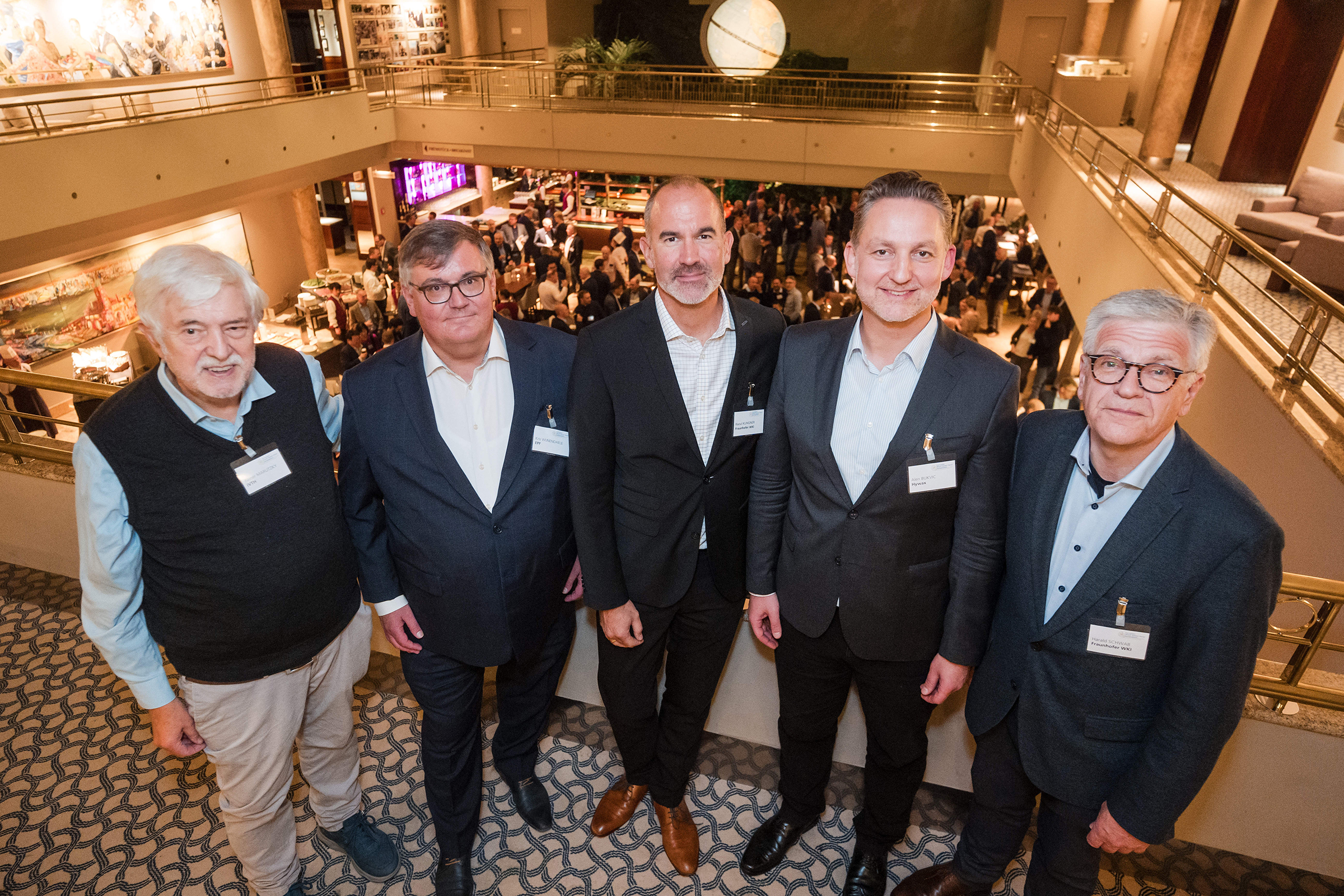 Das Foto zeigt eine Gruppe von fünf Männern in einem festlichen Tagungssaal voller Menschen.