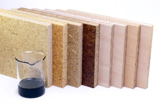 The photo shows four small pieces of chipboard and four pieces of plywood with different colored surfaces as well as a beaker with a dark brown liquid.