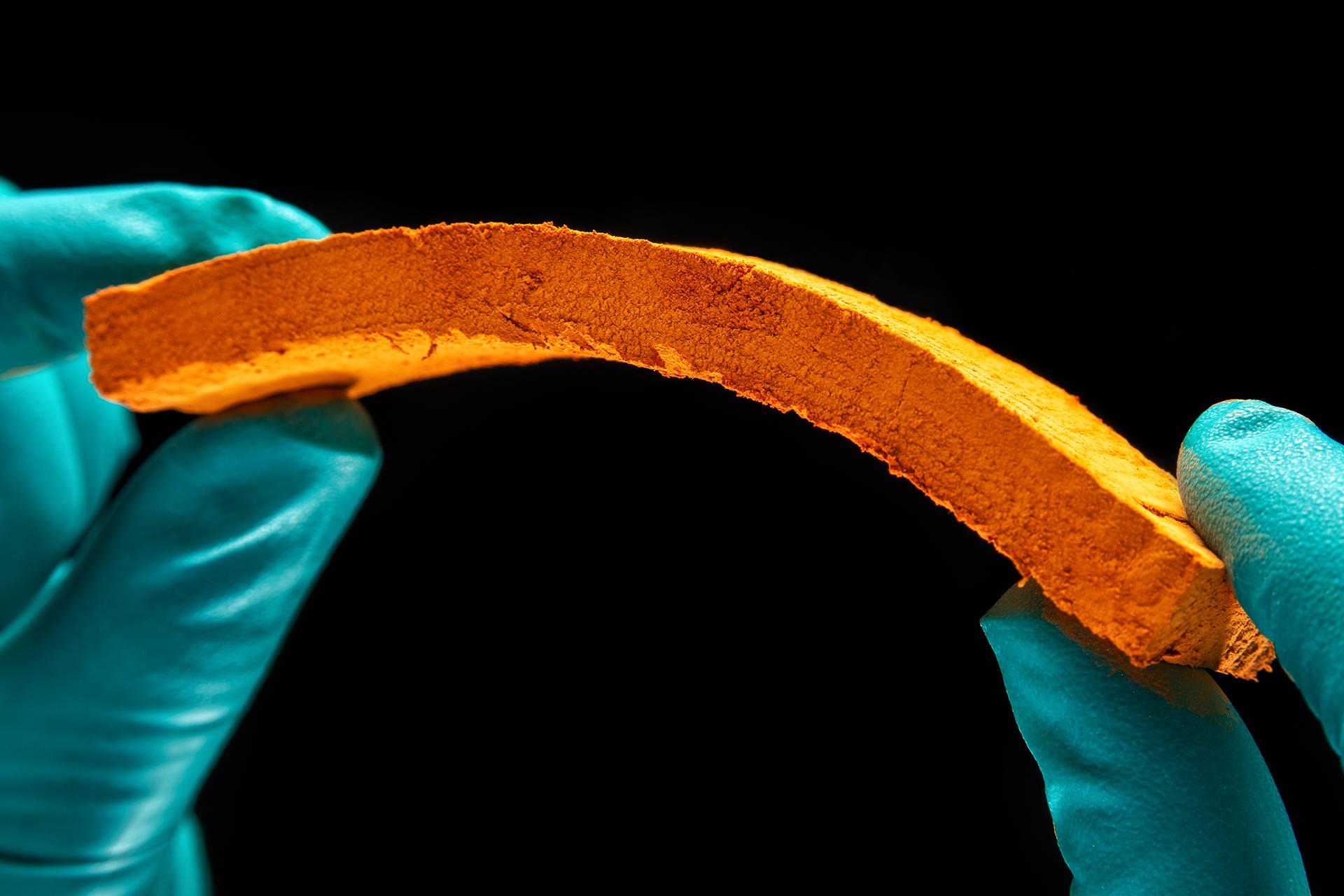 The photo shows two gloved hands bending a piece of aerogel material.