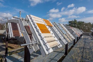 The photo shows a metal framework in the open air, equipped with a large number of wooden parts which are coated in different colors and inclined at an angle towards the sky.