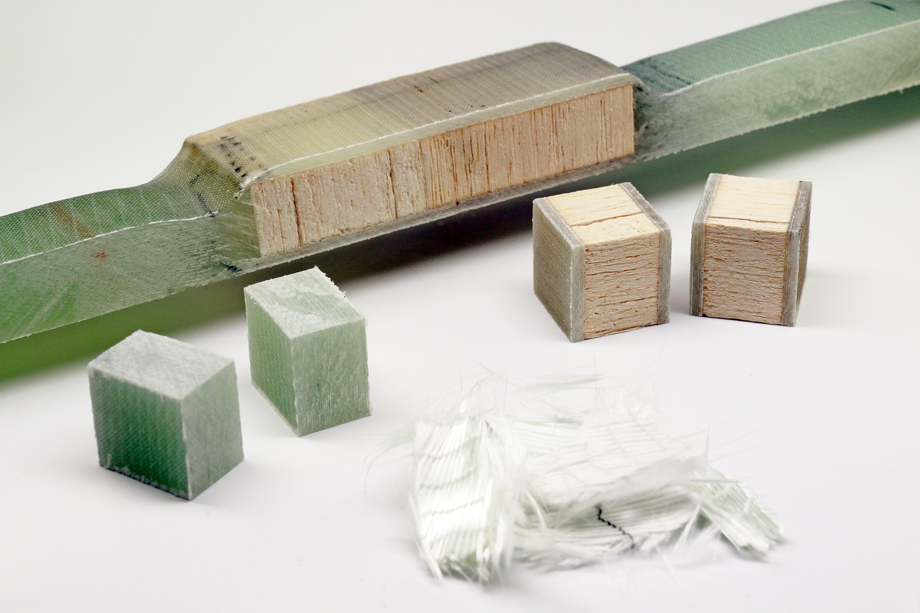 The photo shows, lying next to one another: a small piece of white glass-fiber fabric, and balsa-wood blocks that are embedded in a greenish plastic layer.