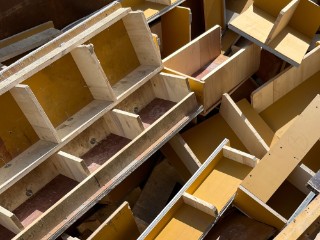 The photo shows a large pile of old molds for concrete formwork. They consist of various wood-based materials bonded together, both coated and uncoated.