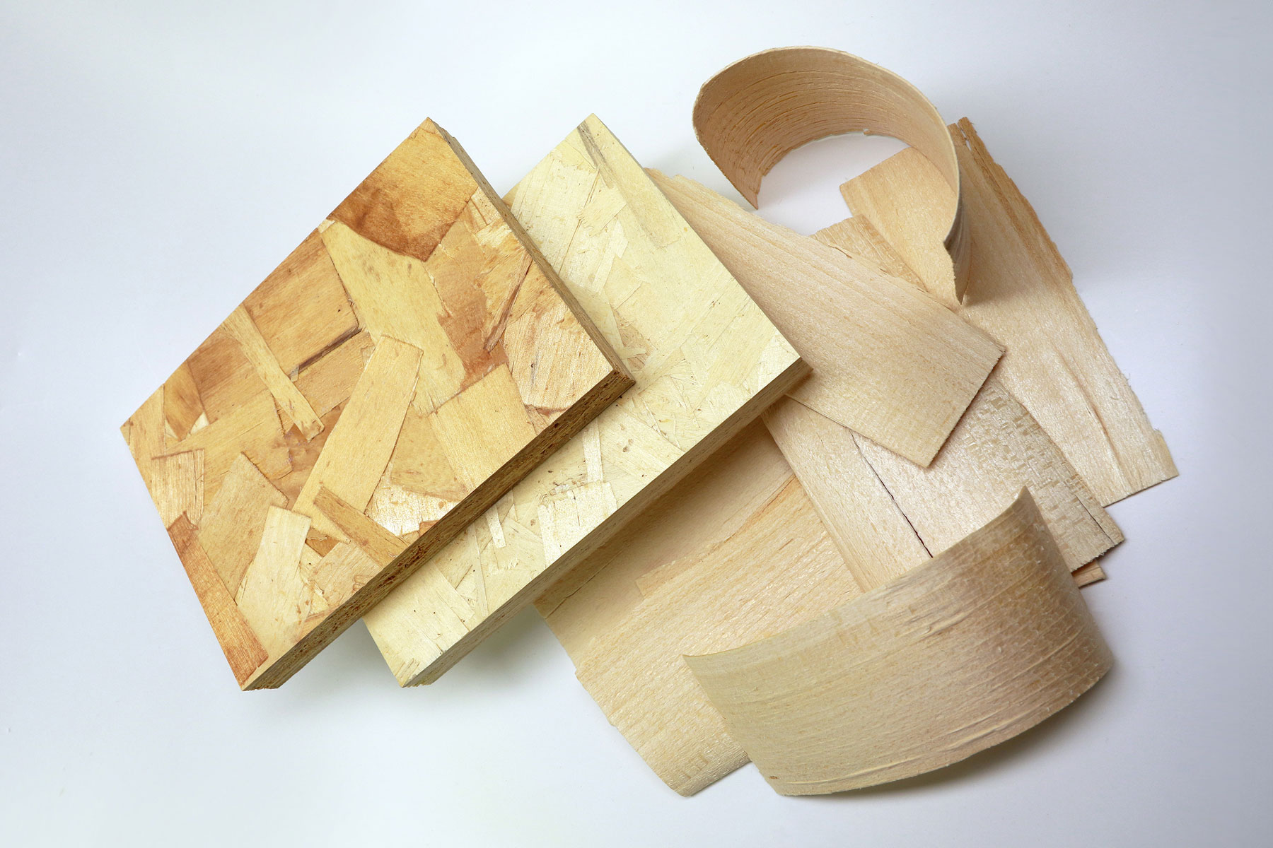 The photo shows two OSB board pieces made from light and slightly darker wood as well as a pile of coarse chips (“strands”) made from hardwood.