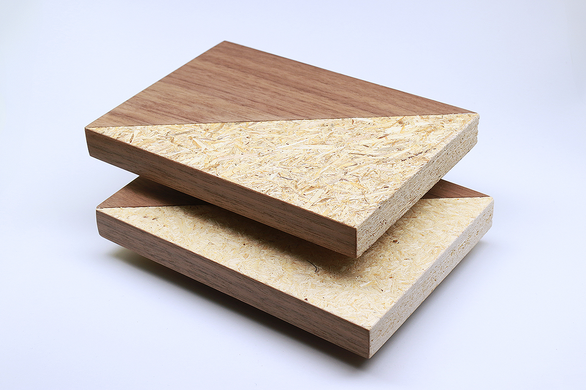 The photo shows two partially veneered pieces of particle board that look almost identical. Some of the wood chips on the upper board are slightly darker. 